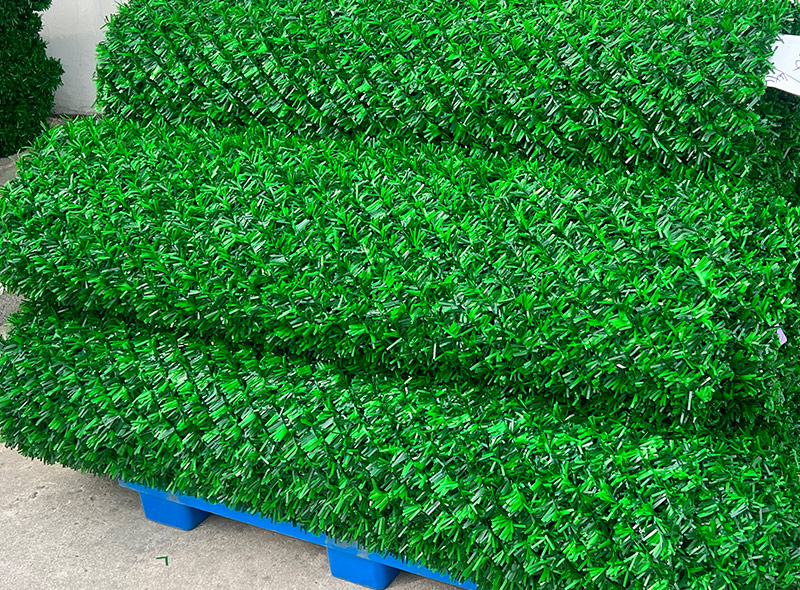 Stacked green artificial hedge panels on a blue pallet, ready for installation.