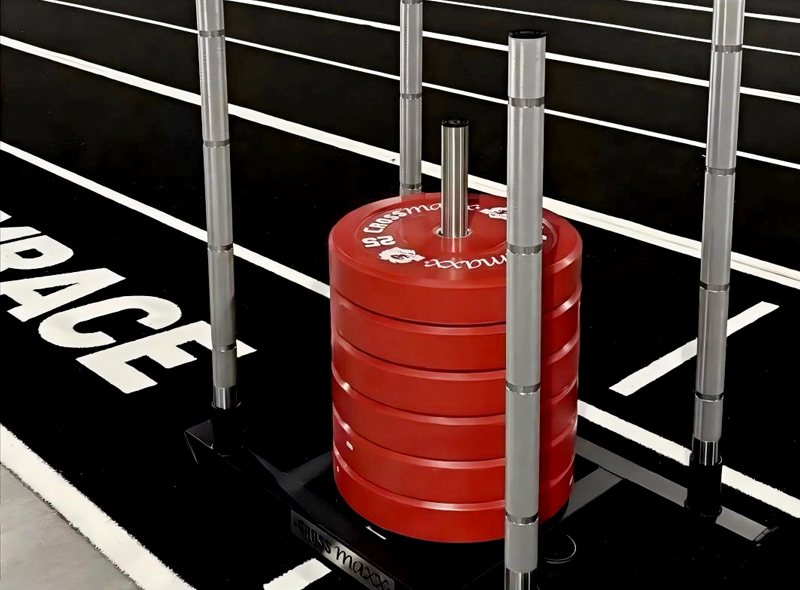 Stack of red bumper plates loaded on a weight plate tree next to a squat rack in a gym. This setup sits on a black floor with white markings.