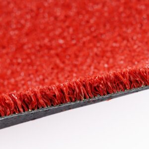 Close-up of red carpet fibers along the edge with a dark backing visible underneath