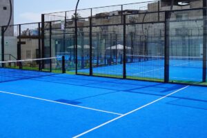 Padel artificial grass court in blue with glass walls, central net and black fencing
