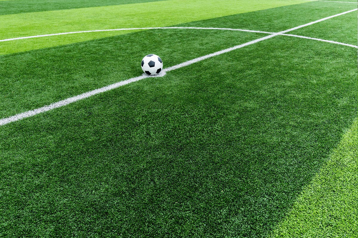 Soccer ball resting on a green turf with white field lines nearby.