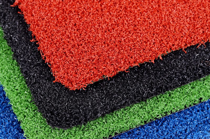 Stack of colorful textured floor mats in red, black, green, and blue, stacked diagonally for display.