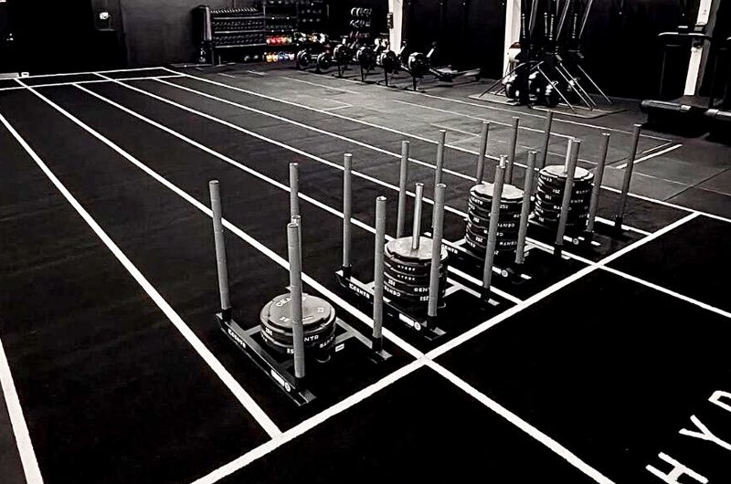 Industrial gym scene with stacked weight plates on racks and white lane markings on a dark floor for lifting workouts.